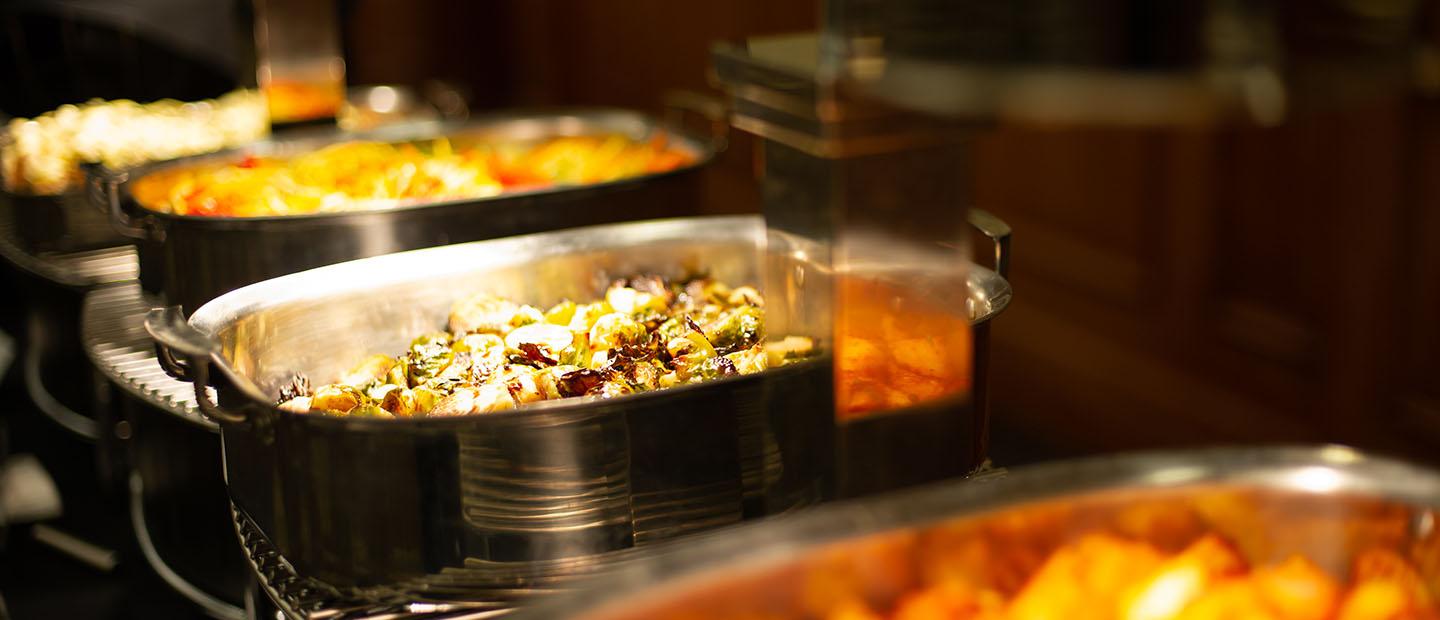 A row of silver dishes full of a variety of catered food.