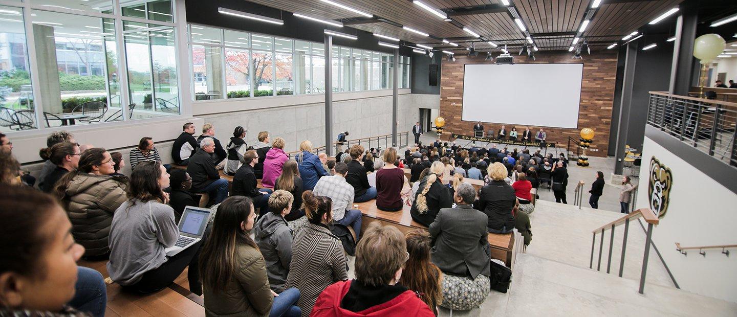 panel of people seated in front of a large white screen, facing an audience